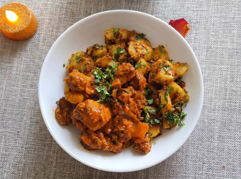 A white bowl filled with chicken curry and spiced potatoes, garnished with fresh cilantro.
