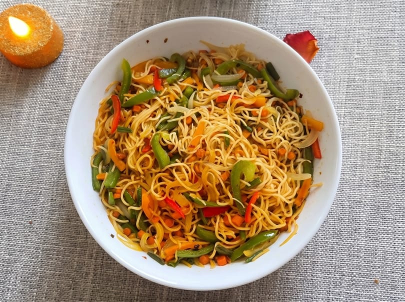 A white bowl filled with vegetable noodles, featuring colorful bell peppers, carrots, and onions.
