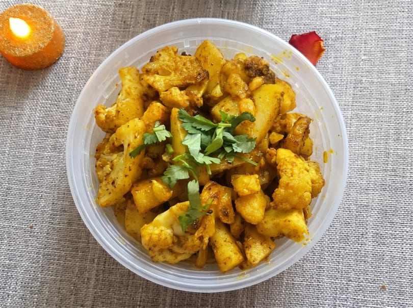 A plastic container of aloo gobi, garnished with cilantro, next to a lit candle.
