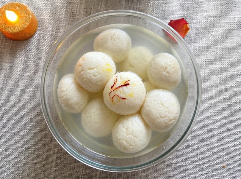 A glass bowl of Rasgulla, a traditional Indian sweet, with saffron strands and a lit candle.